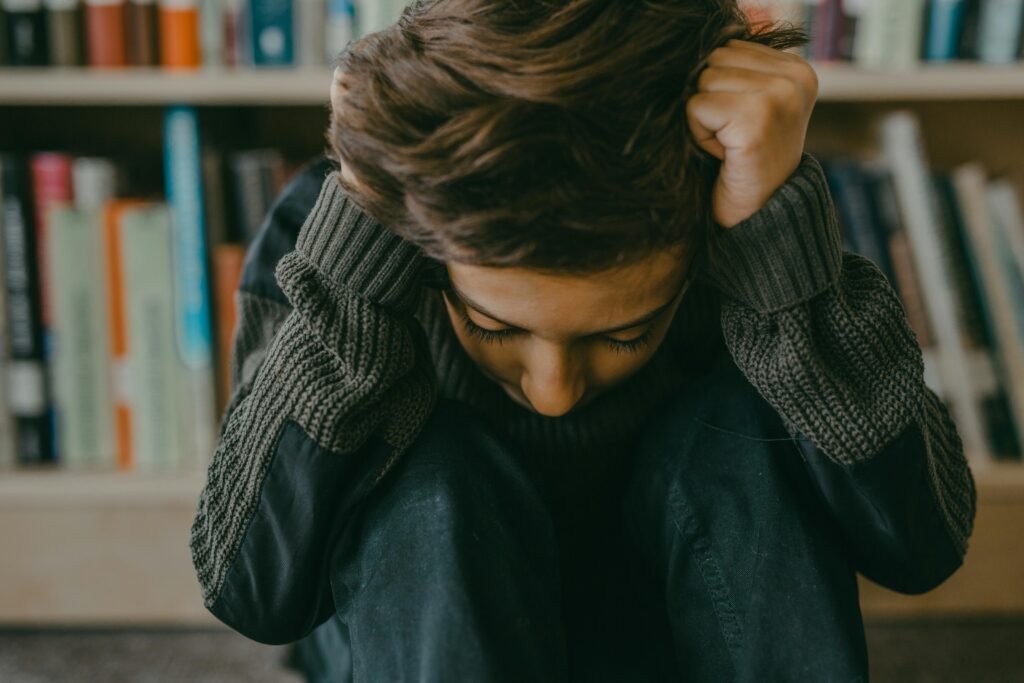 A young person sitting in a thoughtful, introspective pose in a library setting.